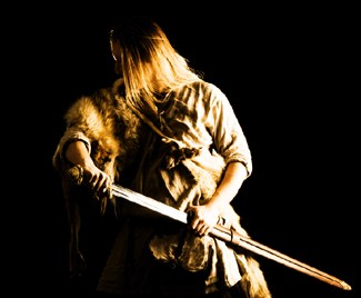A dramatic low-key portrait of a figure in furs holding a spear