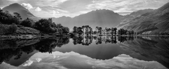 A high-contrast black and white landscape of mountains reflected in a still lake