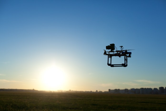 A camera-equipped helicopter drone silhouetted against a sunset sky